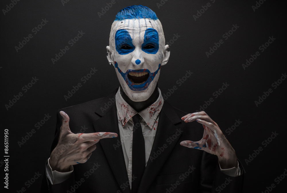 Terrible clown and Halloween theme: Crazy blue clown in black suit isolated on a dark background in the studio
