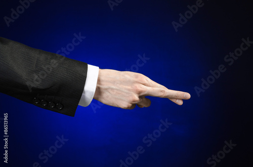 Businessman and gesture topic: a man in a black suit and white shirt showing hand gesture on an isolated dark blue background in studio © Parad St