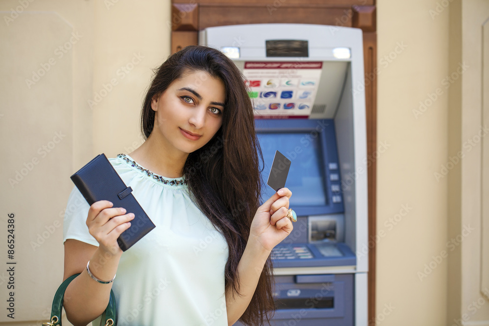 Young woman in jeans short using an automated teller machine Young woman in jeans short using an automated teller machine