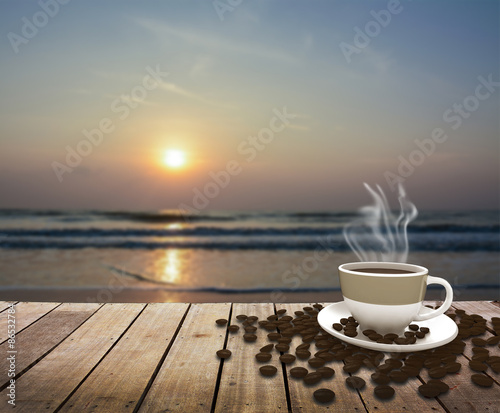 Cup with coffee on table over sea at sunrise