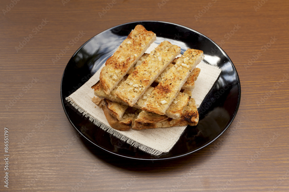 Garlic bread on black plate with space on wood background Garlic bread on black plate with space on wood background
