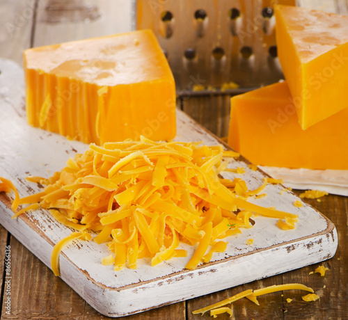 Grated Cheddar Cheese on  wooden Cutting Board.