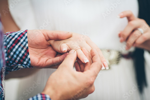 A groom gently holding a gold ring on his brides hand