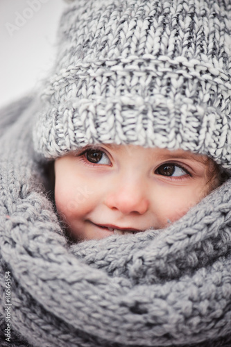 happy baby girl in oversize knitted grey scarf in winter forest