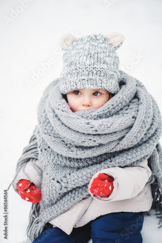 cute baby girl in oversize knitted grey scarf in winter forest