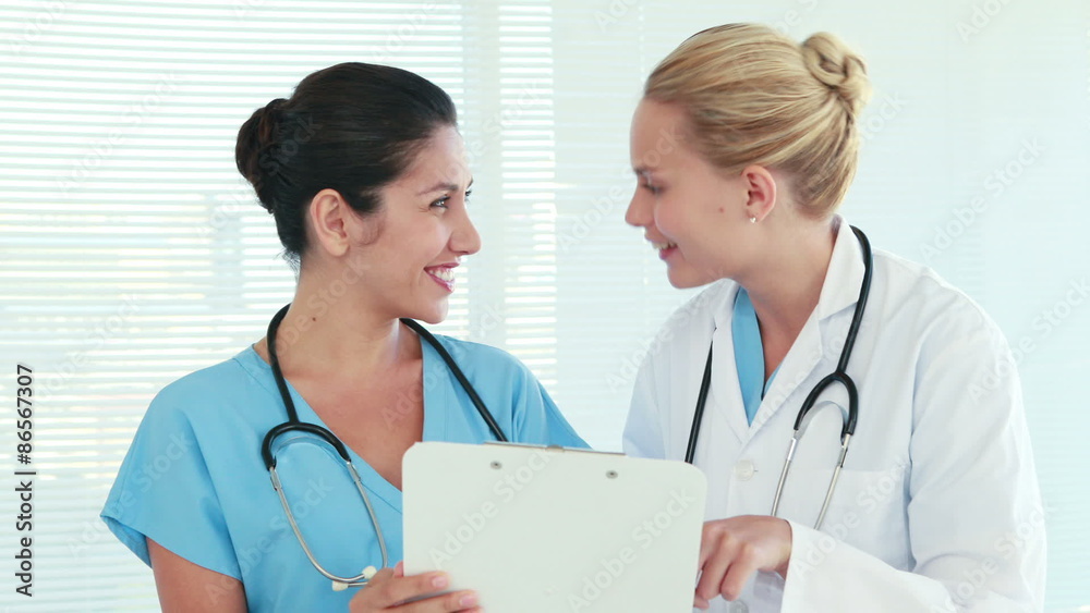 Two doctors speaking together and looking at clipboard Two doctors speaking together and looking at clipboard