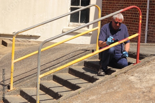 A painter painting handrails along a walkway with concrete steps