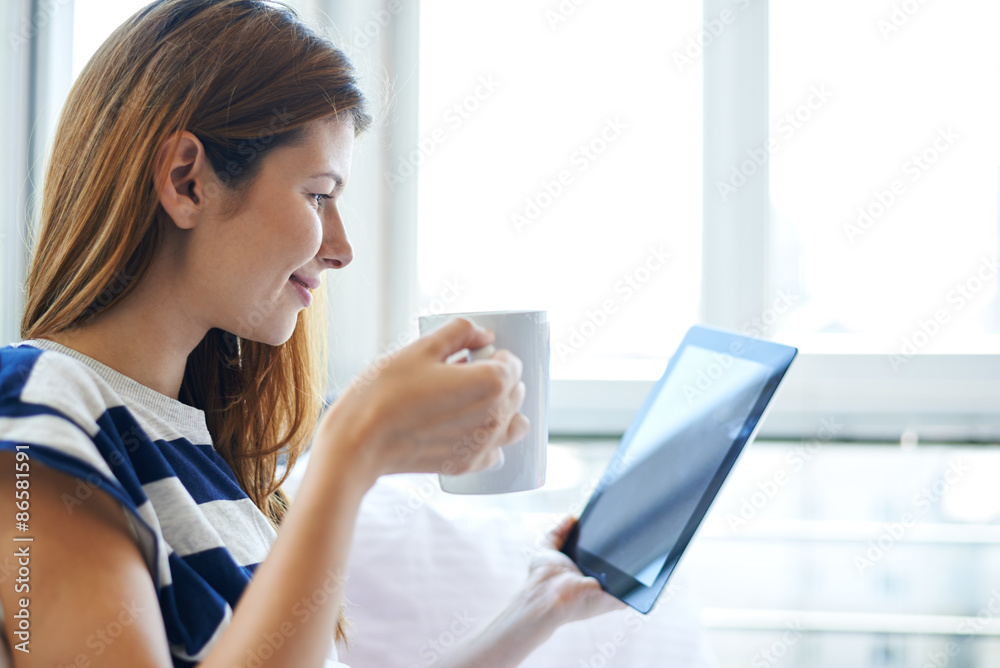 Young woman drinking coffee and reading digital tablet in bed Young woman drinking coffee and reading digital tablet in bed