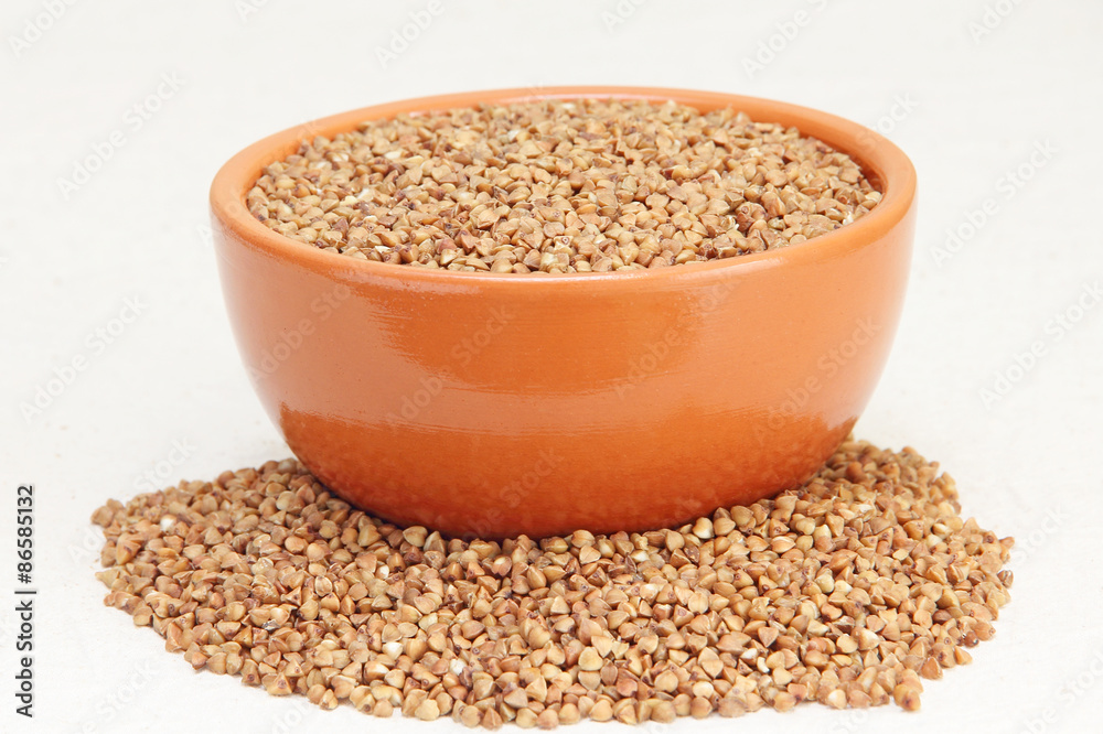 Buckwheat in brown ceramic bowl on a white fabric. Buckwheat in brown ceramic bowl on a white fabric.
