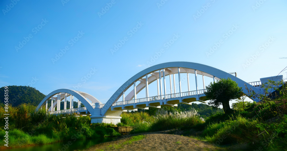 old arch bridge across the creek in LAMPHUN THAILAND. White color arch bridge with blue sky