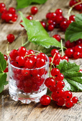 Fresh red currants with leaves in glass on a wooden table, selec