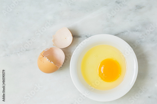 one egg yolk in white bowl and broken egg shells