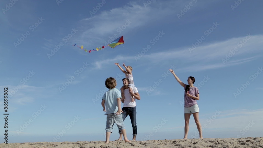 A family of four are playing with a kite. The mother is flying it and the children are chasing after it.