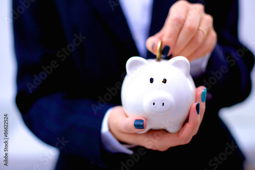 Businesswoman putting money into a piggy bank isolated on white
