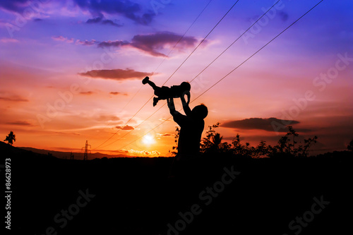  silhouettes of father and son play at mountain range and high voltage electricity pylon sunset background