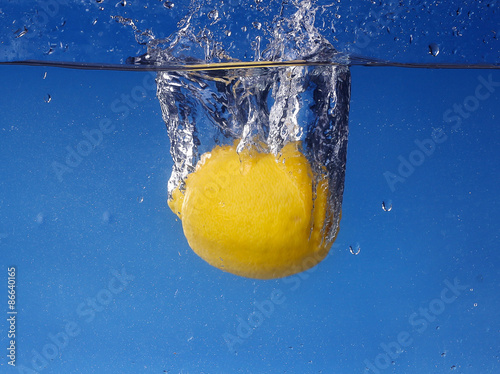 Whole lemon dropped in water against gradient blue background