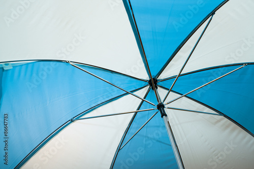 A close up  abstract view of the inside of an open  blue white colored umbrella covered in raindrops