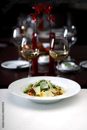 Pasta with arugula and parmesan with glass of white wine in background, shallow depth of field