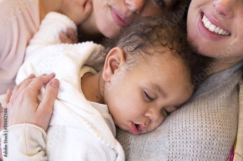 Same sex female couple lying down with their baby son photo