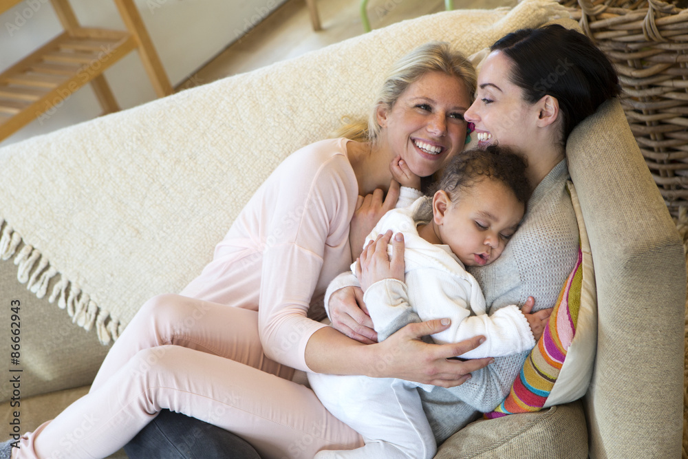 Same sex female couple cuddling on the sofa with their sleeping son