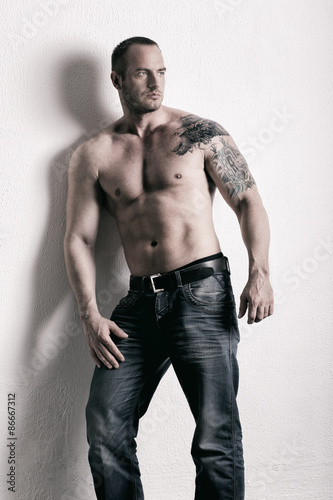 Man posing shirtless, leaning on white wall