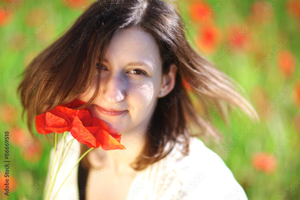 Naklejka premium Young atractive woman standing among blooming poppies on a sunny day
