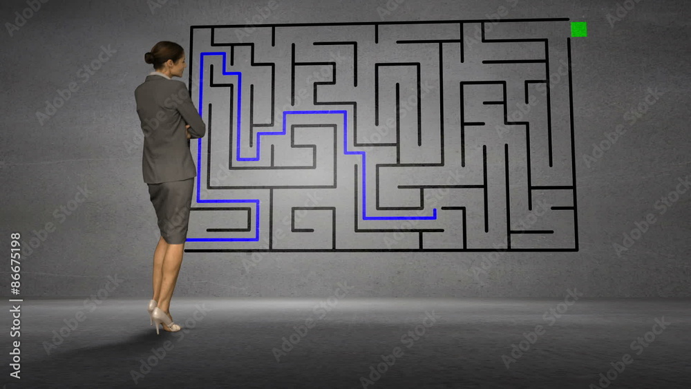 Businesswoman looking at grey wall with maze Businesswoman looking at grey wall with maze