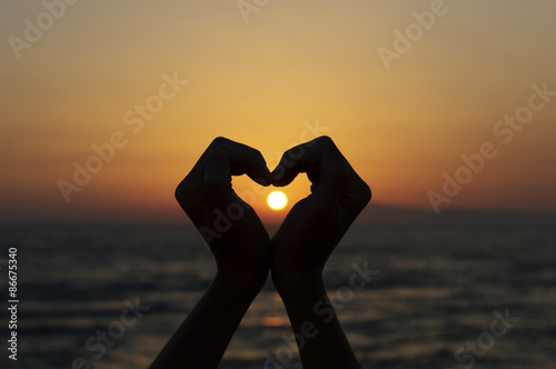 heart shape silhouette made with hands against sunset