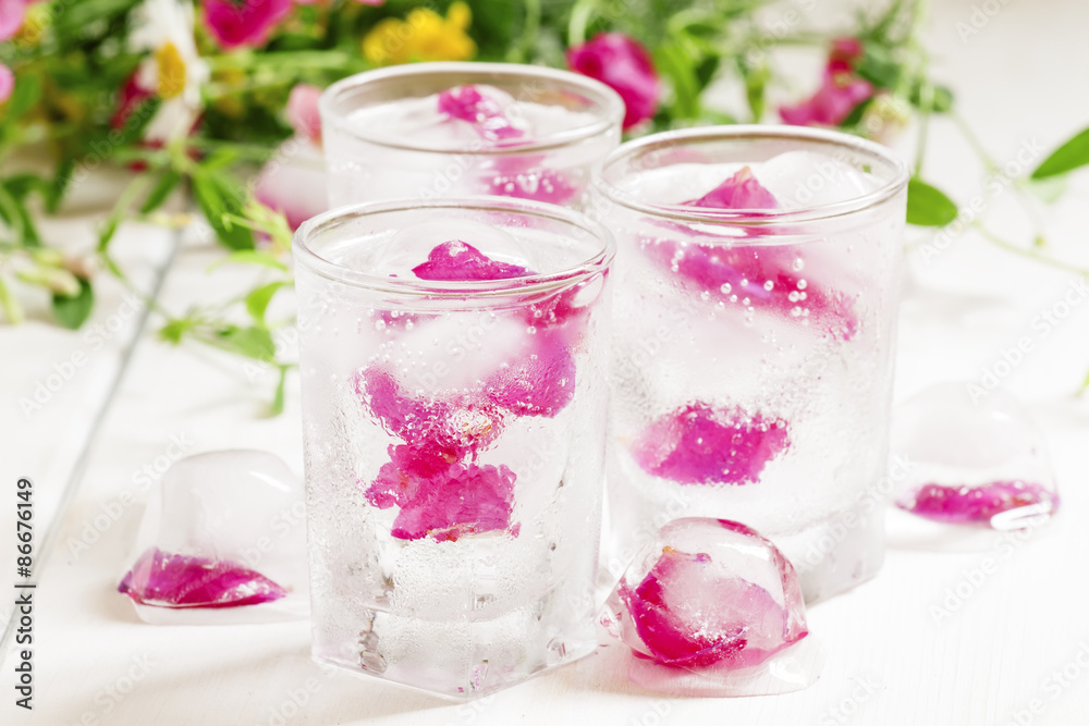 Fresh sparkling beverage with ice with rose petals on white wood Fresh sparkling beverage with ice with rose petals on white wood