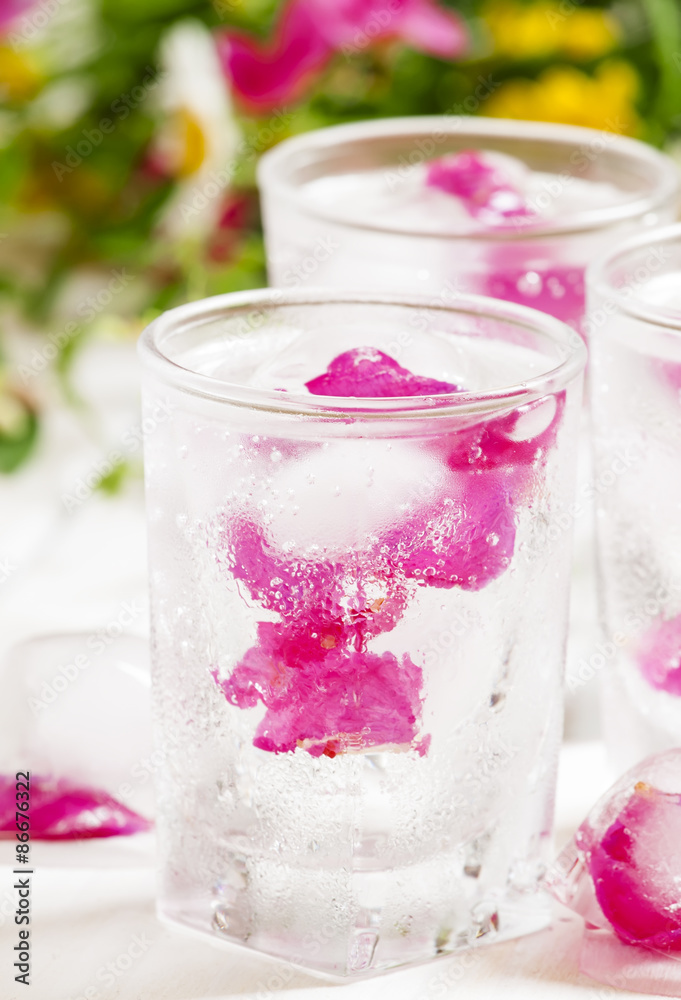 Fresh sparkling beverage with ice with rose petals on white wood Fresh sparkling beverage with ice with rose petals on white wood