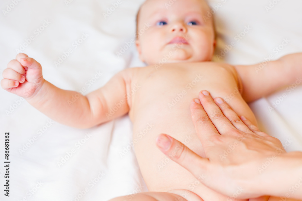 Mother makes baby massage with happy newborn at white bed Mother makes baby massage with happy newborn at white bed