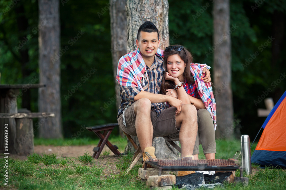 Young couple wrapped in blanket warming up by the fire in front of the tent Young couple wrapped in blanket warming up by the fire in front of the tent