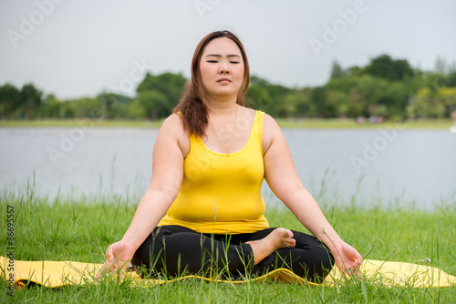 Beautiful relax fatty woman meditating in garden near river