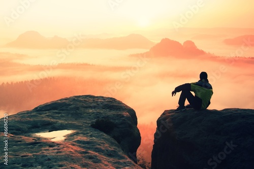 Rear view of male hiker sitting on the rocky peak  while enjoying a colorful daybreak above mounrains valley photo