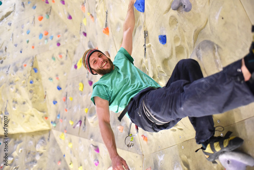 glücklicher Sportler in einer Kletterhalle // 
climber hanging on a wall and smiling photo