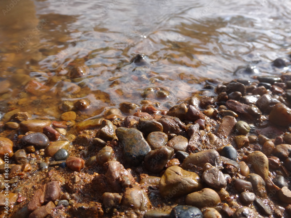 Камни галька в воде с коричневым оттенком в солнечный день