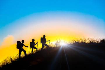 People meeting sunrise on team building session Group of people silhouettes walking toward mountain summit with backpacks hiking trekking gear meeting uprising sun sunbeams and blue sky of background