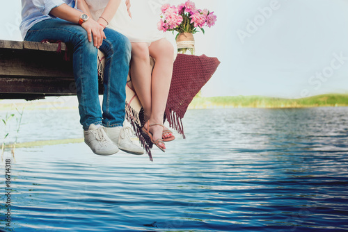 Fotografia Pretty strong young loving couple sitting on the bridge over the river, next to