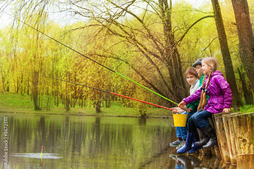 Children sitting and fishing together near pond