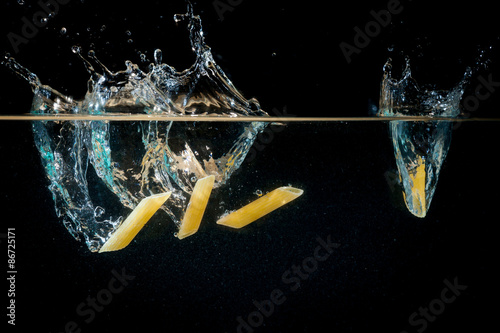 Fotografia Pennette, pasta cade nell'acqua bollente, generando schizzi e bolle d'aria