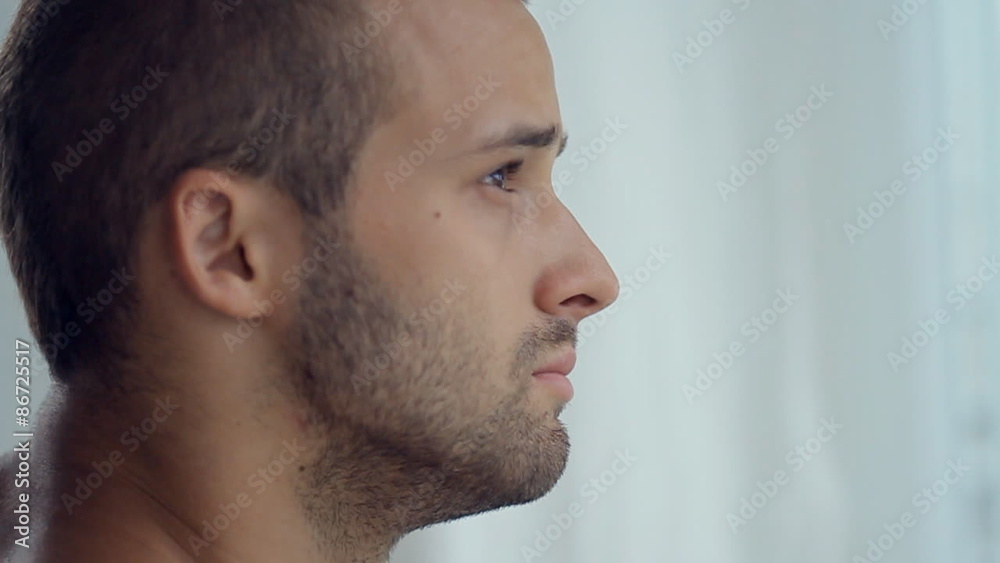 The bearded shirtless man standing near the window and drinking The bearded shirtless man standing near the window and drinking