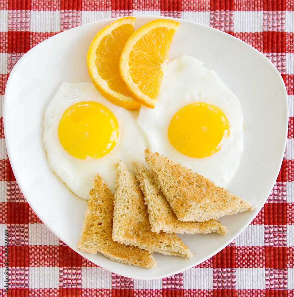 Fototapeta premium Breakfast Eggs Sunny Side Up – A breakfast plate with two sunny side up eggs, toast, and orange slices.