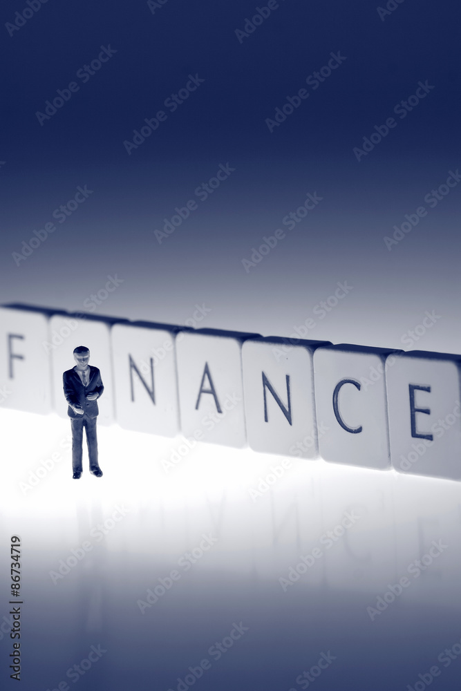 Fototapeta premium Miniature businessman finance. Miniature scale model businessman standing in front of the word finance on tiles.