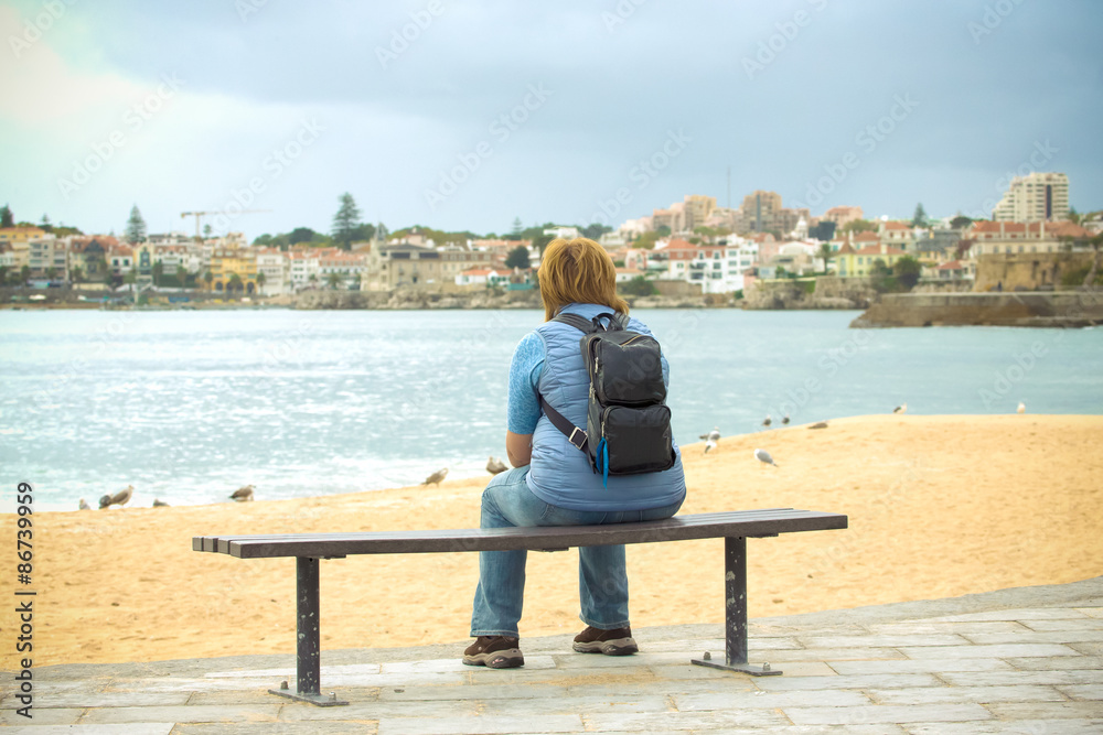 Girl with a backpack sitting on the coast and looking to the opp
