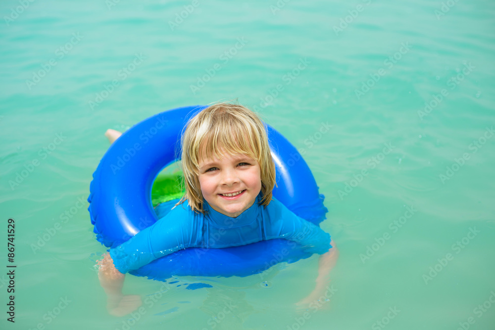 Smiling little boy  with blue life ring has fun in the water