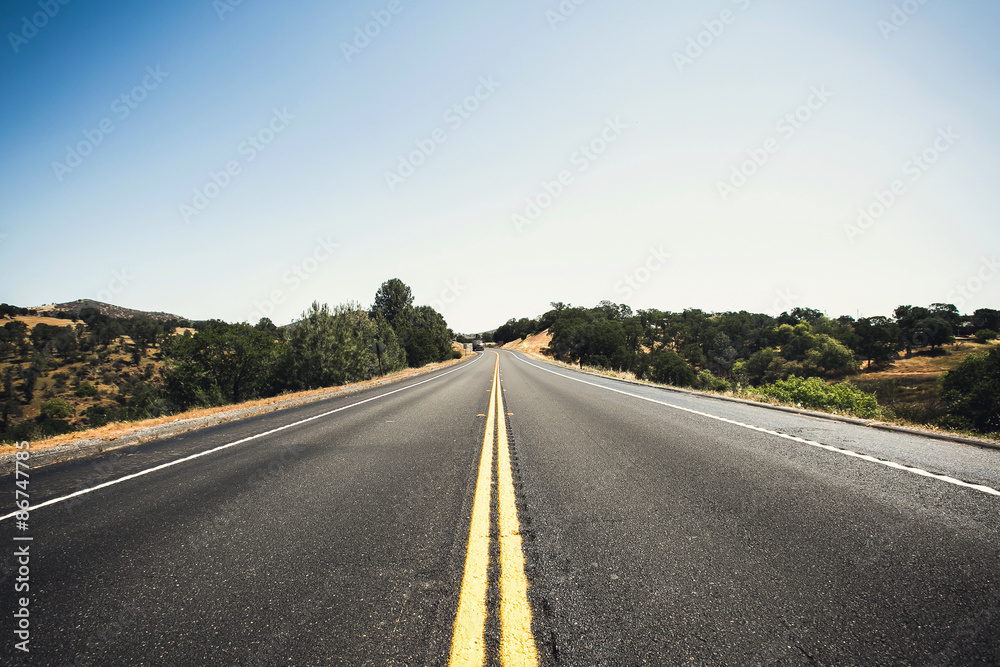 Highway road in California with blue sky above, long road stretching out into the distance

