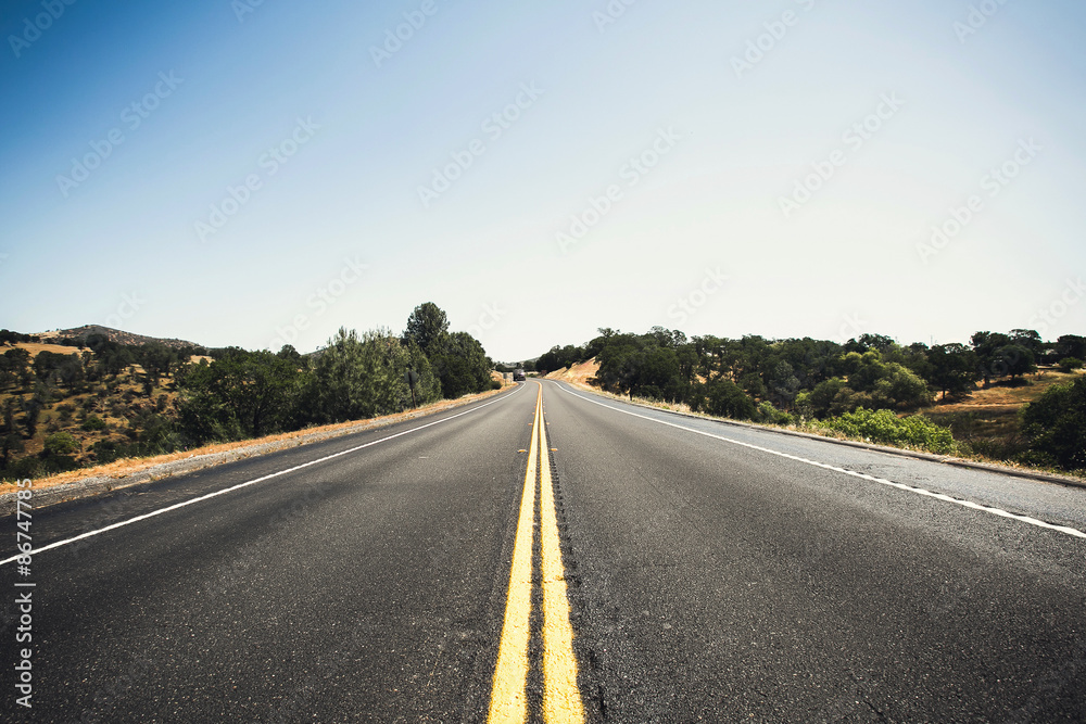 Highway road in California with blue sky above, long road stretching out into the distance
Highway road in California with blue sky above, long road stretching out into the distance