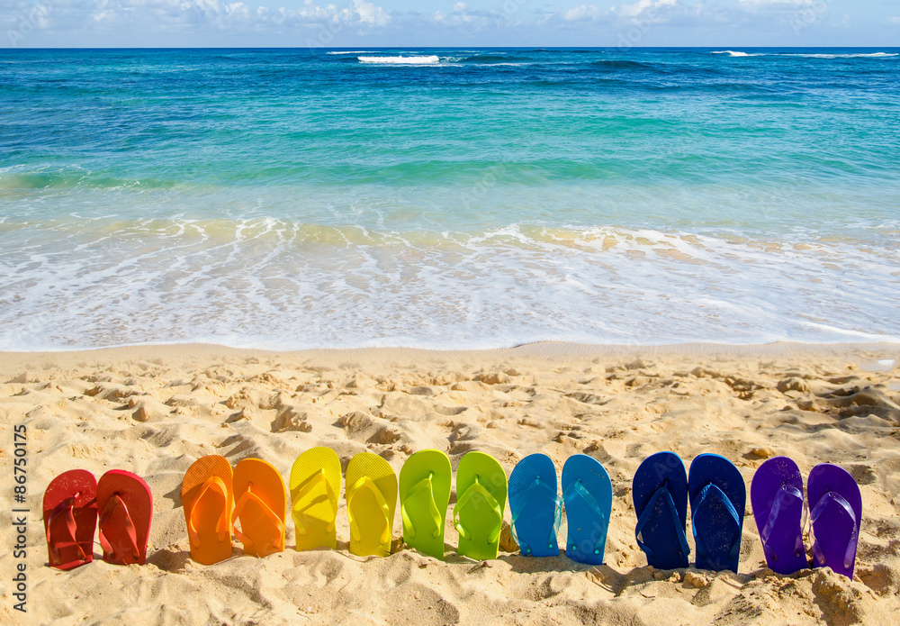 Naklejka premium Colorful flip flops on the sandy beach