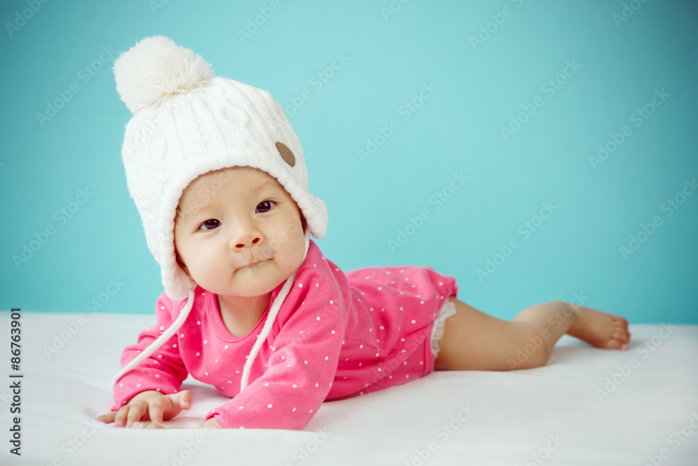 Baby wearing white knitted beanie in front of blue background Baby wearing white knitted beanie in front of blue background