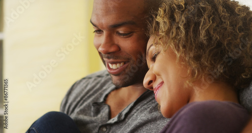Black couple sitting on couch smiling © rocketclips